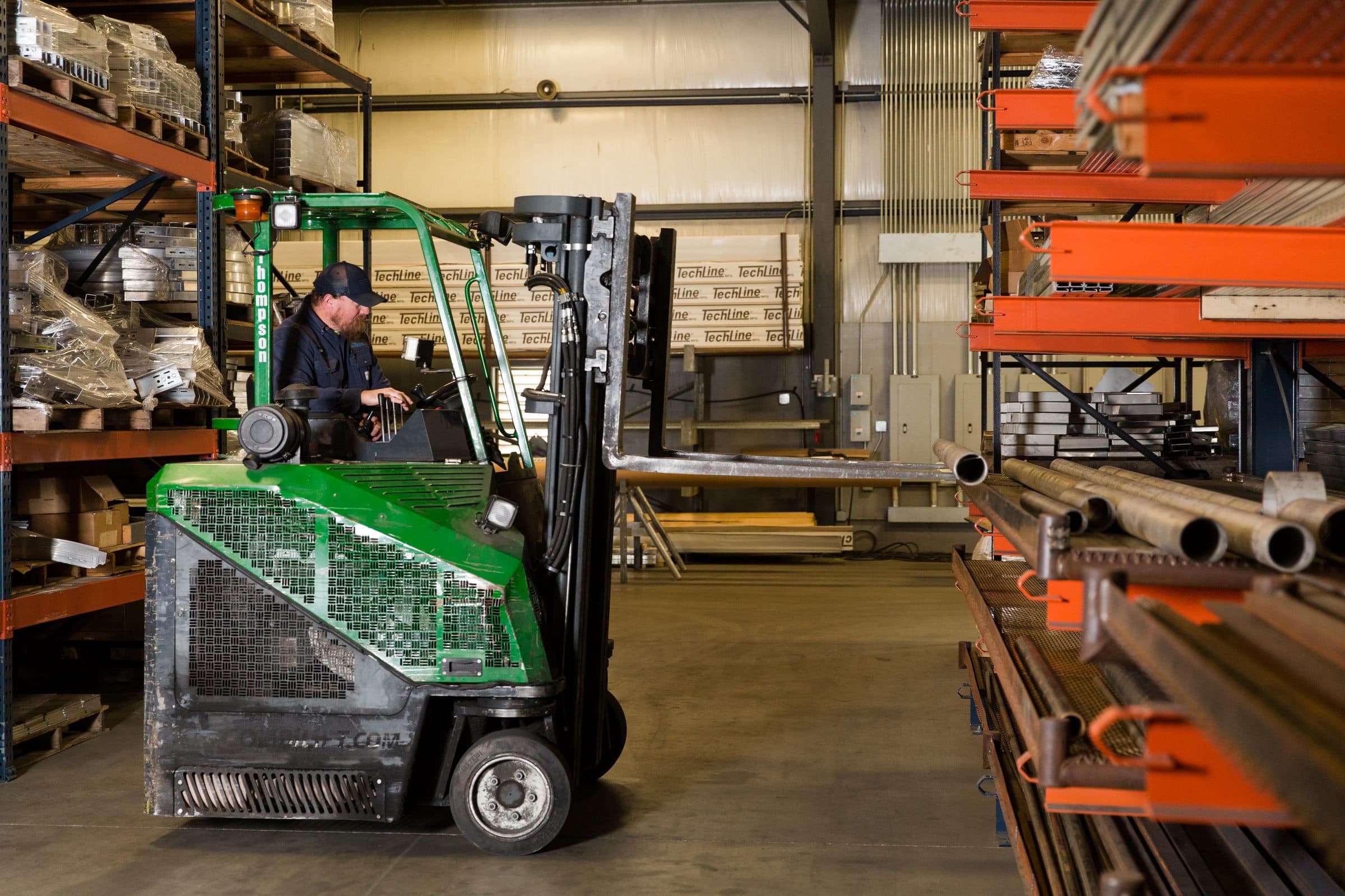 TechLine warehouse worker operating forklift among material storage racks